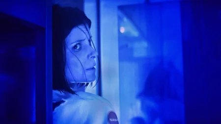 A verdade sombria de A Astronauta: o suspense que paralisou o Prime Video Kate Mara como Sam Walker sentada sozinha em uma casa de quarentena, cercada por sombras e equipamentos médicos, em clima de paranoia.