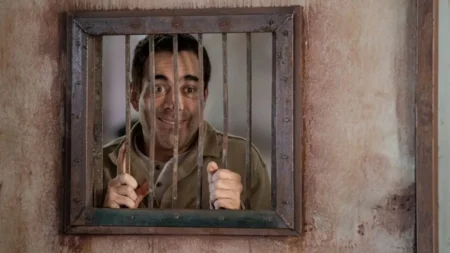 A Cela dos Milagres: final explicado e o sacrifício que muda tudo no filme da Netflix Omar Chaparro como Héctor, com olhar perdido e vulnerável, segurando as grades da prisão em A Cela dos Milagres