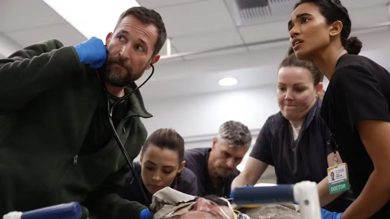 Equipe médica de The Pitt reunida no pronto-socorro em um momento de luto, com expressão abatida e iluminação fria de hospital ao fundo. Equipe médica de The Pitt reunida no pronto-socorro em um momento de luto, com expressão abatida e iluminação fria de hospital ao fundo.