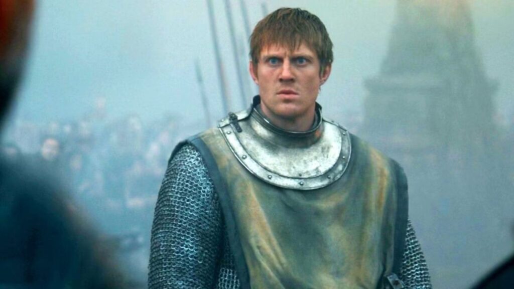 Dunk em armadura diante da multidão durante o Julgamento dos Sete, com Baelor Targaryen ao fundo em clima tenso e sombrio.
